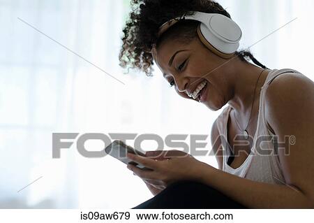 Stock Photo - Woman wearing headphones, looking at smartphone, laughing. Fotosearch