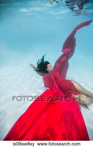 Stock Photo - Woman wearing red dress, draped in red fabric, floating underwater. Fotosearch