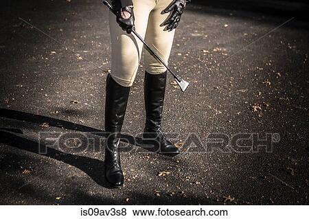 Stock Photo - Woman wearing riding boots, holding riding crop, low section. Fotosearch