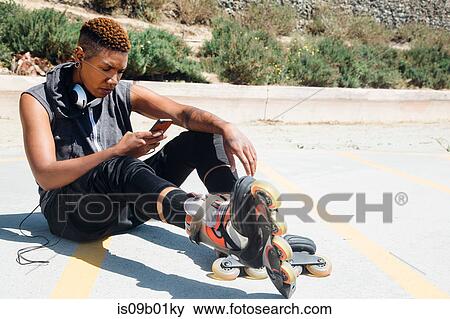 Woman wearing rollerblades and headphones sitting on floor looking at smartphone View Large Photo Image Stock Photo - Woman wearing rollerblades and headphones sitting on floor looking at smartphone. Fotosearch