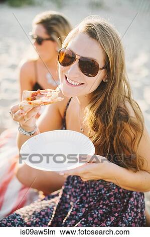 Woman wearing sunglasses eating a slice of pizza looking at camera smiling View Large Photo Image Picture - Woman wearing sunglasses eating a slice of pizza looking at camera smiling. Fotosearch