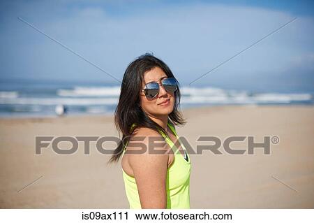 Stock Image - Woman wearing sunglasses on beach looking at camera. Fotosearch