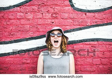 Woman wearing sunhat and sunglasses, in front of mural, mouth open View Large Photo Image Stock Photograph - Woman wearing sunhat and sunglasses, in front of mural, mouth open. Fotosearch