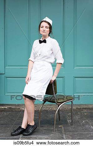 Picture - Woman wearing waitress uniform leaning against chair. Fotosearch