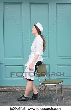 Stock Image - Woman wearing waitress uniform leaning against chair. Fotosearch