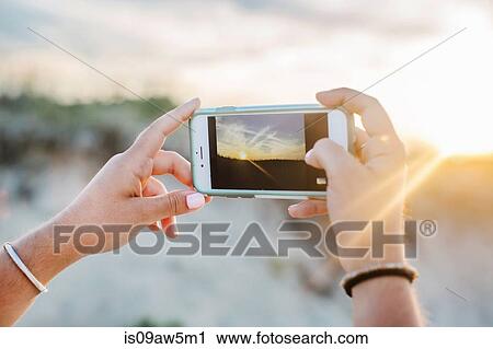 Stock Image - Womans hands using smartphone to photograph vapour trails. Fotosearch