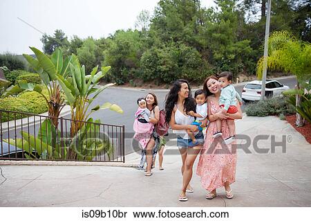 Stock Photography - Women carrying baby daughter and sons moving up driveway, Malibu, California, USA. Fotosearch
