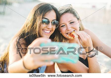 Women eating pizza using smartphone to take selfie smiling View Large Photo Image Picture - Women eating pizza using smartphone to take selfie smiling. Fotosearch