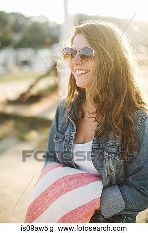 Stock Image - Women wearing denim jacket and sunglasses holding blanket looking away smiling. Fotosearch