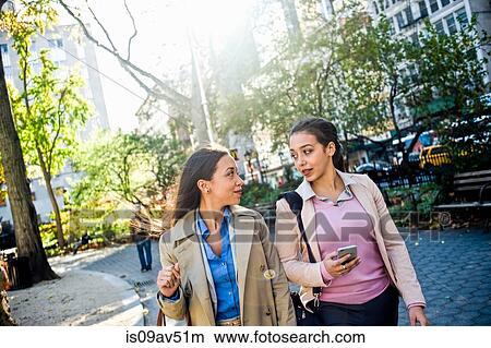 Young adult female twins chatting and walking through city park View Large Photo Image Picture - Young adult female twins chatting and walking through city park. Fotosearch