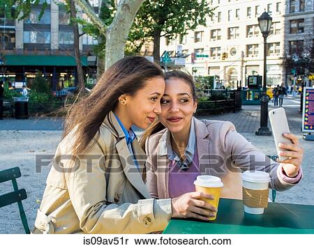 Stock Photography - Young adult female twins taking selfie in city park. Fotosearch