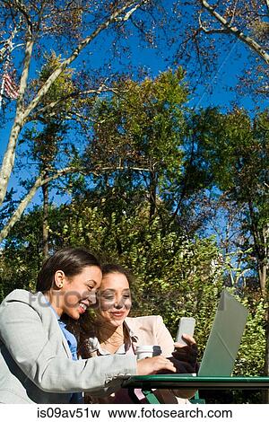 Young adult female twins using laptop and smartphone in city park View Large Photo Image Stock Photo - Young adult female twins using laptop and smartphone in city park. Fotosearch
