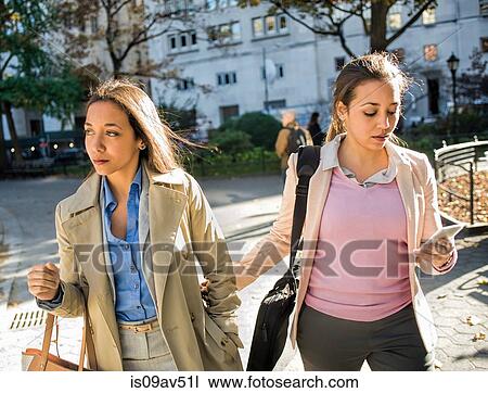 Stock Image - Young adult female twins walking arm in arm through city park. Fotosearch