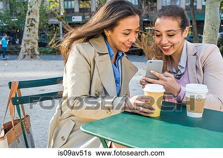 Young adult female twins with takeaway coffee reading smartphone texts in city park View Large Photo Image Stock Photograph - Young adult female twins with takeaway coffee reading smartphone texts in city park. Fotosearch