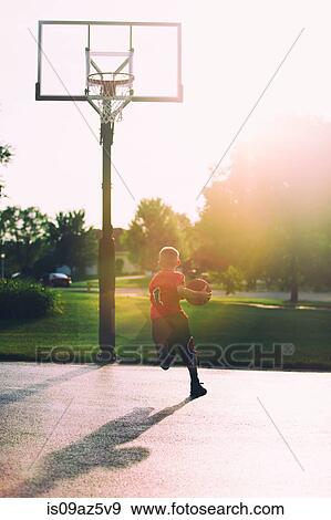 Young boy on basketball court, holding basketball, mid layup, rear view View Large Photo Image Stock Photo - Young boy on basketball court, holding basketball, mid layup, rear view. Fotosearch