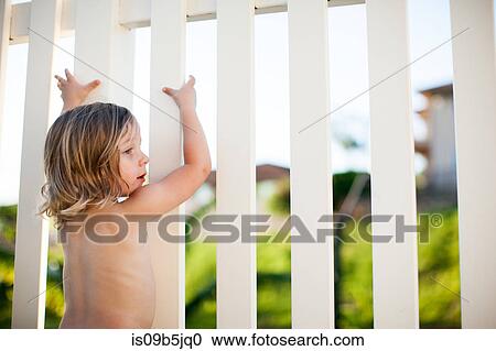 Stock Image - Young boy outdoors, holding onto white fence. Fotosearch