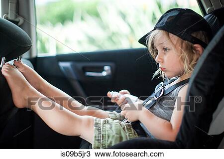 Stock Image - Young boy sitting in child's seat in back seat of car, bored expression. Fotosearch