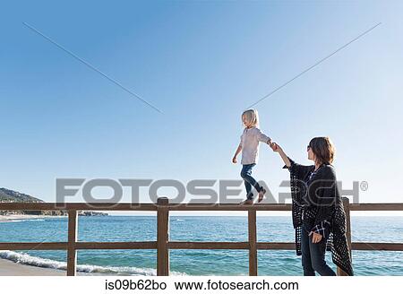 Young boy walking along fence, holding mother's hand, Laguna Beach, California, United States, North America View Large Photo Image Picture - Young boy walking along fence, holding mother's hand, Laguna Beach, California, United States, North America. Fotosearch