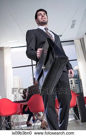 Stock Image - Young businessman carrying briefcase in hotel lobby. Fotosearch