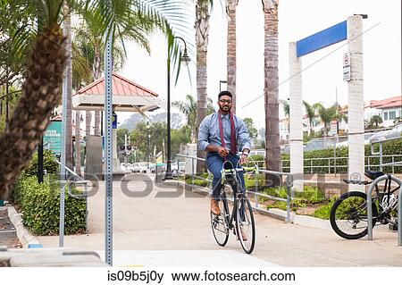 Stock Photo - Young businessman cycling hands free on rail station platform. Fotosearch