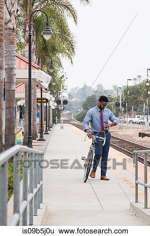 Young businessman cyclist looking at watch on railway station platform View Large Photo Image Stock Photograph - Young businessman cyclist looking at watch on railway station platform. Fotosearch