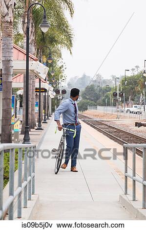 Stock Photo - Young businessman cyclist looking back from rail station platform. Fotosearch