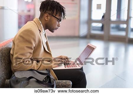 Stock Photo - Young businessman sitting in train station typing on laptop. Fotosearch