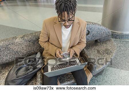 Young businessman sitting in train station using smartphone and laptop View Large Photo Image Stock Photo - Young businessman sitting in train station using smartphone and laptop. Fotosearch