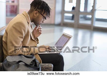 Young businessman sitting in train station typing on laptop View Large Photo Image Stock Photograph - Young businessman sitting in train station typing on laptop. Fotosearch