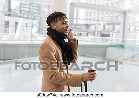 Stock Image - Young businessman talking on smartphone in train station atrium. Fotosearch