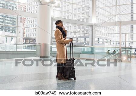 Young businessman with wheeled case talking on smartphone in train station atrium View Large Photo Image Stock Photo - Young businessman with wheeled case talking on smartphone in train station atrium. Fotosearch