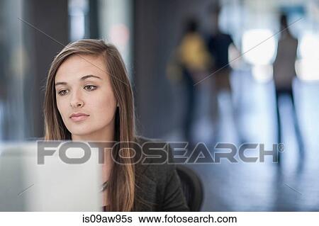 Young businesswoman sitting at desk, using computer View Large Photo Image Stock Photograph - Young businesswoman sitting at desk, using computer. Fotosearch