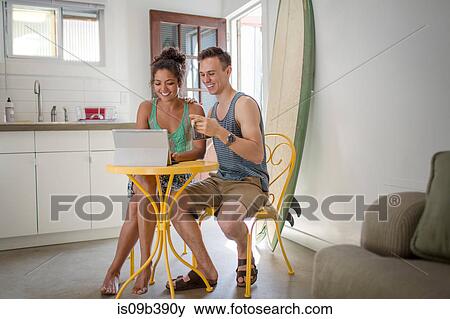 Young couple at kitchen table using laptop View Large Photo Image Stock Photo - Young couple at kitchen table using laptop. Fotosearch