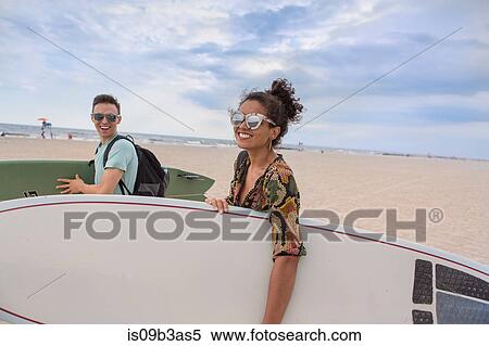 Stock Photography - Young couple carrying surfboards on Rockaway Beach, New York State, USA. Fotosearch