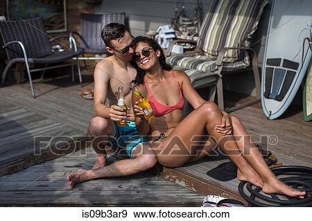 Young couple in bikini and swimming shorts with bottles of beer on porch, Rockaway Beach, New York State, USA View Large Photo Image Stock Photo - Young couple in bikini and swimming shorts with bottles of beer on porch, Rockaway Beach, New York State, USA. Fotosearch