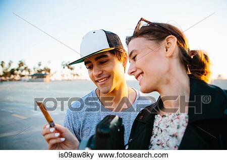 Young couple looking at instant photograph at coast, Venice Beach, California, USA View Large Photo Image Stock Photo - Young couple looking at instant photograph at coast, Venice Beach, California, USA. Fotosearch