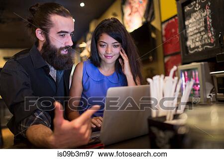 Young couple pointing at laptop at public house table View Large Photo Image Stock Photo - Young couple pointing at laptop at public house table. Fotosearch