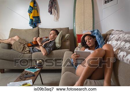Stock Photo - Young couple relaxing on sofa using digital tablet and playing guitar. Fotosearch