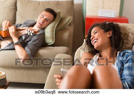 Stock Photo - Young couple relaxing on sofa using digital tablet and playing guitar. Fotosearch