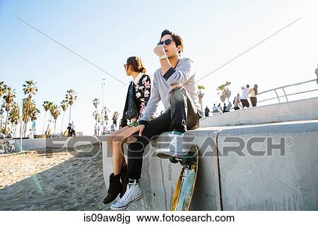 Young couple sitting on wall, man resting foot on skateboard View Large Photo Image Stock Image - Young couple sitting on wall, man resting foot on skateboard. Fotosearch