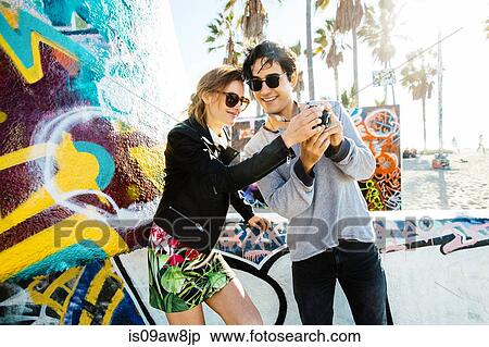 Young couple standing by graffiti art, looking at back of digital camera View Large Photo Image Stock Photography - Young couple standing by graffiti art, looking at back of digital camera. Fotosearch