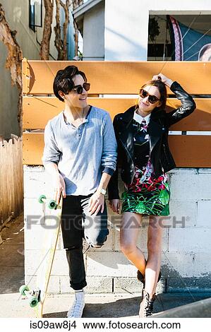 Young couple standing together outdoors, young man holding skateboard View Large Photo Image Picture - Young couple standing together outdoors, young man holding skateboard. Fotosearch