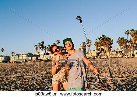Picture - Young couple taking selfie with smartphone stick on beach, Venice Beach, California, USA. Fotosearch