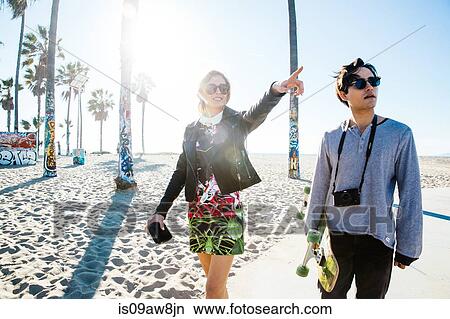 Young couple walking along beach walkway, young woman pointing View Large Photo Image Picture - Young couple walking along beach walkway, young woman pointing. Fotosearch