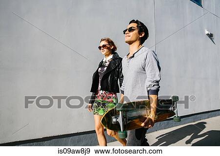 Young couple walking together outdoors, man carrying skateboard View Large Photo Image Stock Photo - Young couple walking together outdoors, man carrying skateboard. Fotosearch