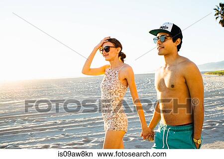 Young couple wearing swimming costume and shorts strolling on beach, Venice Beach, California, USA View Large Photo Image Picture - Young couple wearing swimming costume and shorts strolling on beach, Venice Beach, California, USA. Fotosearch