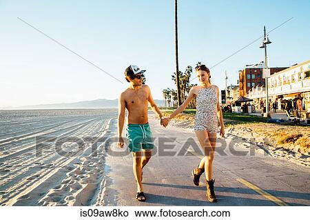 Young couple wearing swimming costume and shorts strolling at beach, Venice Beach, California, USA View Large Photo Image Picture - Young couple wearing swimming costume and shorts strolling at beach, Venice Beach, California, USA. Fotosearch