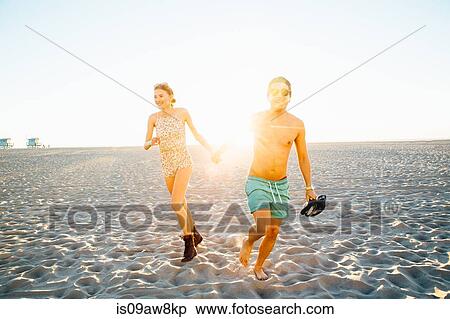 Young couple wearing swimming costume and shorts running on sunlit beach, Venice Beach, California, USA View Large Photo Image Stock Photography - Young couple wearing swimming costume and shorts running on sunlit beach, Venice Beach, California, USA. Fotosearch