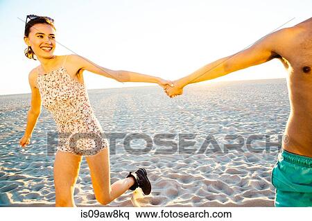 Young couple wearing swimming costume and shorts holding hands on beach, Venice Beach, California, USA View Large Photo Image Stock Photography - Young couple wearing swimming costume and shorts holding hands on beach, Venice Beach, California, USA. Fotosearch