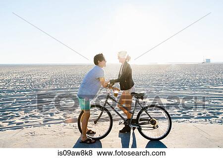 Young couple with bicycle chatting on sunlit beach, Venice Beach, California, USA View Large Photo Image Stock Photo - Young couple with bicycle chatting on sunlit beach, Venice Beach, California, USA. Fotosearch